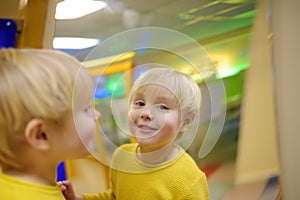 Cute little boy looks in distorting mirror in playcenter