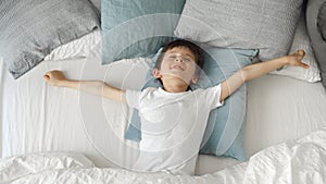 Cute little boy lying in bed, stretching hands and yawn. Child waking up in bed at morning