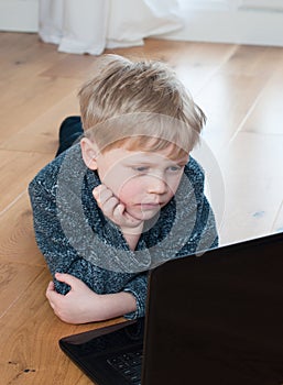 Cute little boy lying on the floor using a laptop