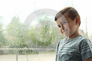 Cute little boy near window indoors. Rainy day