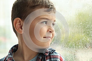 Cute little boy near window indoors. Rainy day