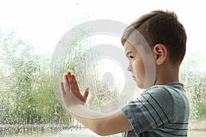 Cute little boy near window indoors. Rainy day