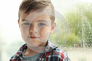 Cute little boy near window indoors. Rainy day