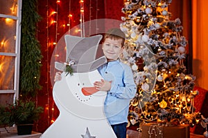 Cute Little Boy opening Gift box under Christmas Tree in red house interior