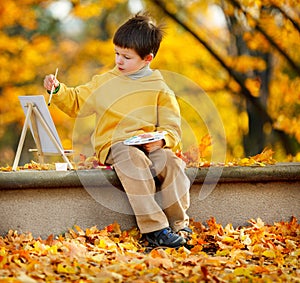 Cute little boy painting in golden autumn park