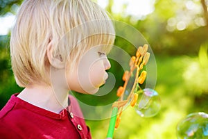 Cute little boy is playing with big bubbles outdoor. Child is blowing big and small bubbles simultaneously