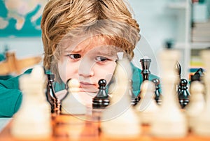 Cute little boy playing chess. Thinking kid. Concentrated boy developing chess strategy, playing board game.