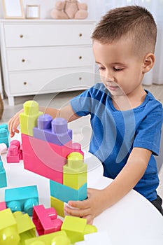 Cute little boy playing with colorful building blocks at table in room