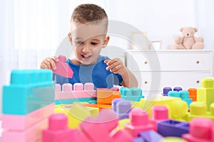 Cute little boy playing with colorful building blocks at table in room