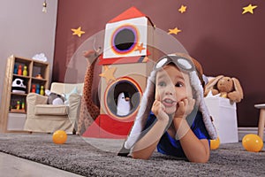 Cute little boy playing on floor near cardboard rocket  at home. Child`s room interior