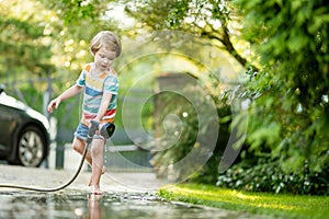 Cute little boy playing with garden hose on hot summer day. Child playing with water at summertime