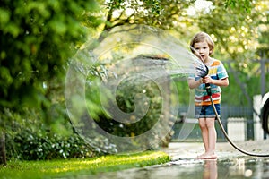 Cute little boy playing with garden hose on hot summer day. Child playing with water at summertime