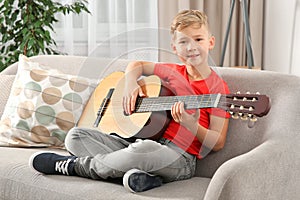 Cute little boy playing guitar on sofa