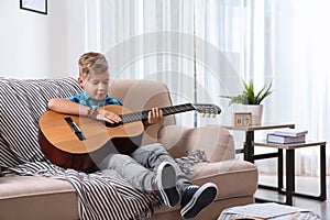 Cute little boy playing guitar on sofa