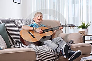 Cute little boy playing guitar on sofa