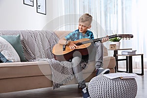 Cute little boy playing guitar on sofa