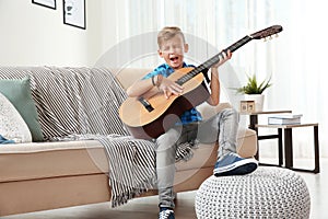 Cute little boy playing guitar on sofa