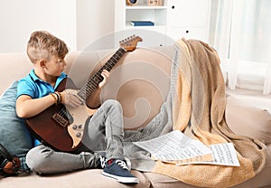 Cute little boy playing guitar on sofa in room.