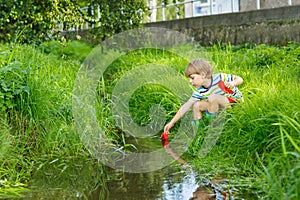 Cute little boy playing with paper boats by a river