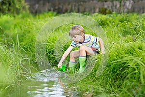 Cute little boy playing with paper boats by a river