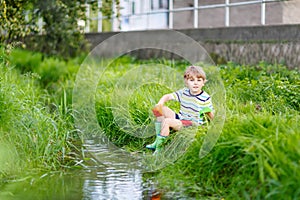 Cute little boy playing with paper boats by a river