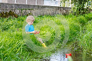 Cute little boy playing with paper boats by a river