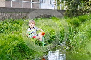 Cute little boy playing with paper boats by a river