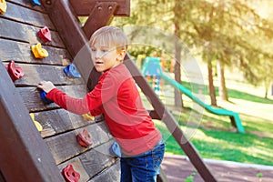 Cute little boy playing on the playground. Happy child climbing on the wooden wall. Happy summer vacation