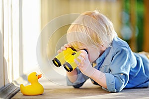 Cute little boy playing with rubber duck and plastic binoculars outdoors