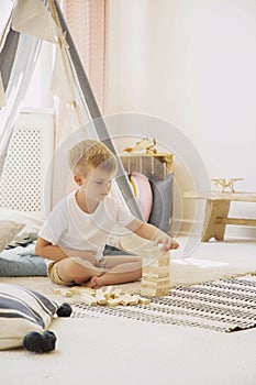 Cute little boy playing with wooden blocks in scandinavian playroom, real photo with copy space on empty wall