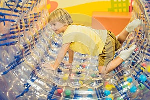 Cute little boy, playing in Zorb a rolling plastic cylinder ring with a hole in the middle, intdoor