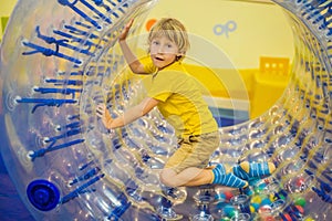 Cute little boy, playing in Zorb a rolling plastic cylinder ring with a hole in the middle, intdoor