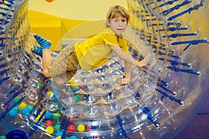 Cute little boy, playing in Zorb a rolling plastic cylinder ring with a hole in the middle, intdoor