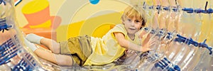 Cute little boy, playing in Zorb a rolling plastic cylinder ring with a hole in the middle, intdoor BANNER, long format