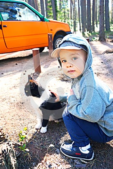 Cute little boy plays with black and white kitten, strokes it against the background of an orange car