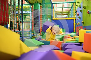 Cute little boy plays with soft cubes in the dry pool in play center. Kid playing on indoor playground in foam rubber pit in