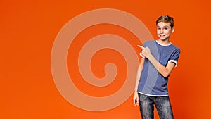 Cute little boy pointing away on orange background