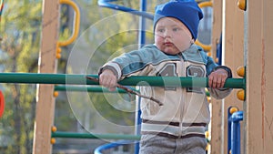 Cute little boy portrait in a blue hat climbs stairs on the playground