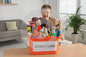 Cute little boy putting toy into donation box at home