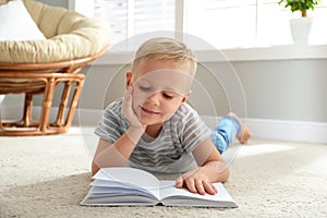 Cute little boy reading book on floor