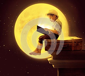 Cute little boy reading a book in the moon light