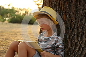 Cute little boy reading book near tree in park