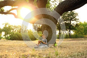 Cute little boy reading book near tree