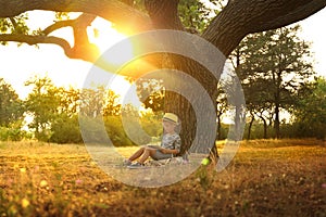 Cute little boy reading book near tree in park