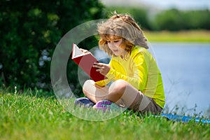 Cute little boy reading book in park. Kid sit on grass and reading book. Kid boy reading interest book in the garden