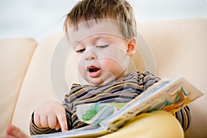 Lindo pequeno chico lectura un libro sobre el sofá 