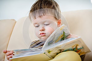 Cute little boy reading book on sofa