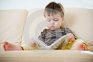 Cute little boy reading book on sofa