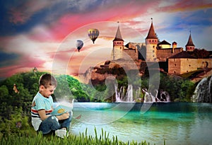 Cute little boy reading magic book near lake and castle on background