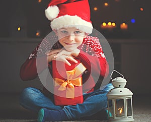 Cute little boy in red hat with gift and  latern waiting Santa Claus